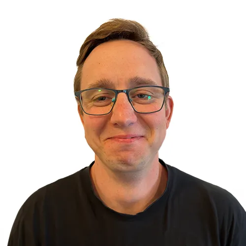 Man med kort brunt hår och glasögon ler, bär svart skjorta mot vit bakgrund.
